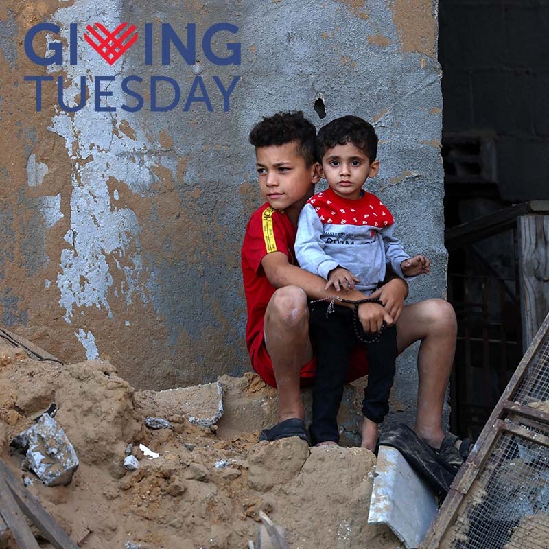 The Giving Tuesday logo is overlaid on an image of two boys sitting together in a pile of rubble.