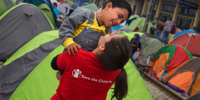 A young child refugee from Syria laughs and plays with Save the Children's Mariluz Garcia in Idomeni at the border between Greece and the Former Yugoslav Republic of Macedonia. More than 10,000 refugees are stranded in Idomeni waiting for the border to open. Save the Children works in Idomeni offering protection to children traveling alone and provides food and support to families. Photo credit: Pedro Armestre, September 2015.