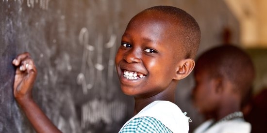 A 9-year-old schoolgirl in Uganda smiles brightly as she practices writing numbers on a chalkboard in her classroom. Photo credit: Jordan. J. Hay, 2012.