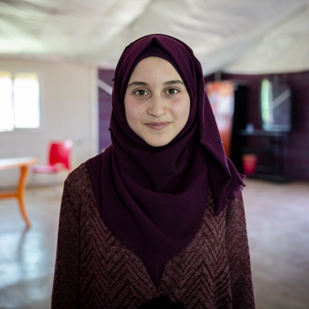 Maya, 14, stands smiling at the camera in her classroom in Za’atori refugee camp in Jordan.