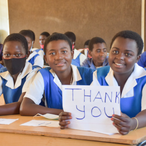 A young female student, Christabel, displaying a thank you placard for Save the Children donors to Malawi.