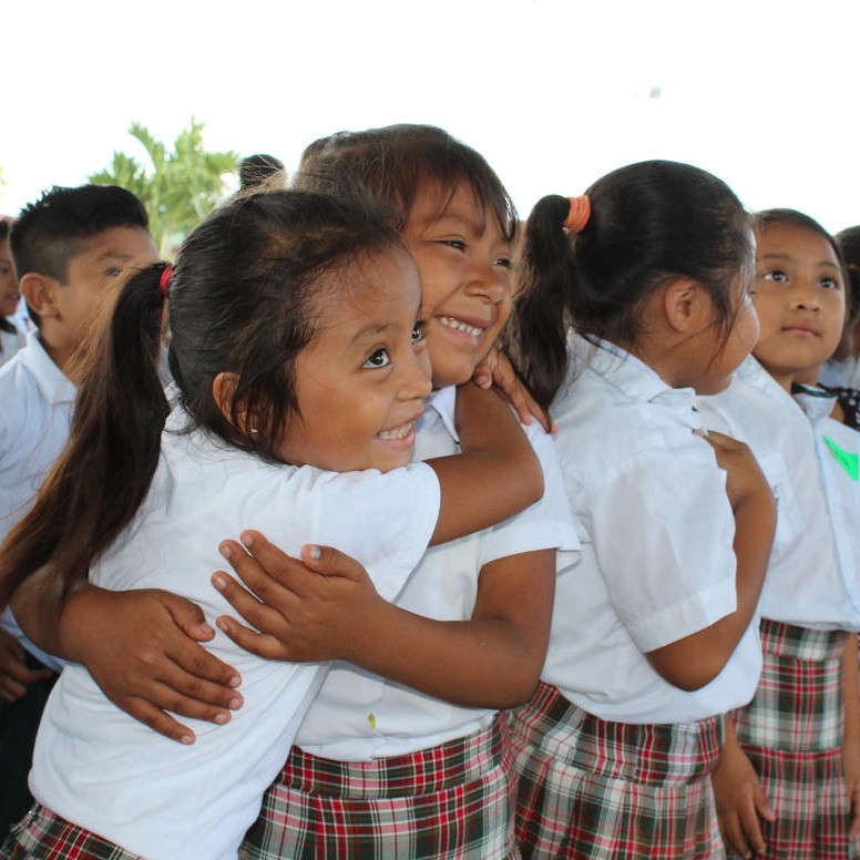 Two young girls from Mexico in their school uniforms happily hug each other.