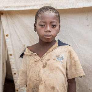A ten-year old African child who lost his home when Cyclone Idai hit stands near a tent in Mozambique.