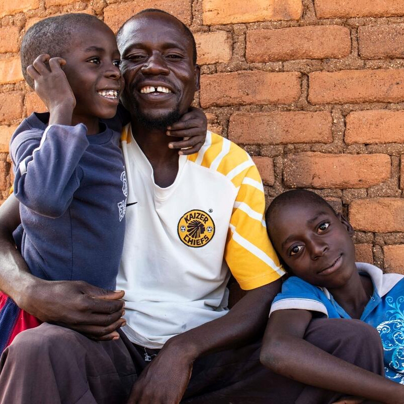 Ntokozo from Zimbabwe smiles as he embraces his sons Joseph, age 7, and Sipho, age 13.