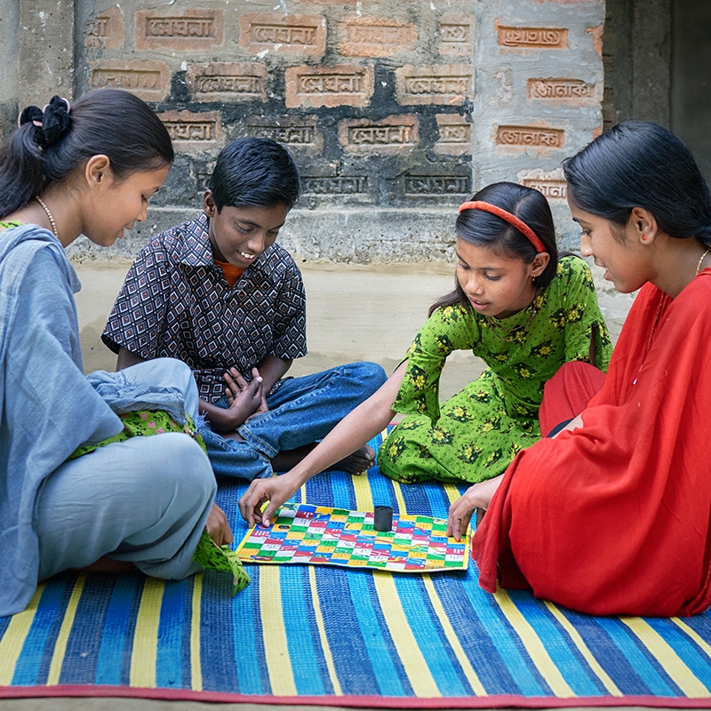 Bangladesh, a group of cousins play a board game outside their house.