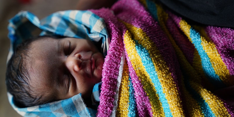 In Bangladesh, a baby is wrapped tighly in a colorful blanket. 