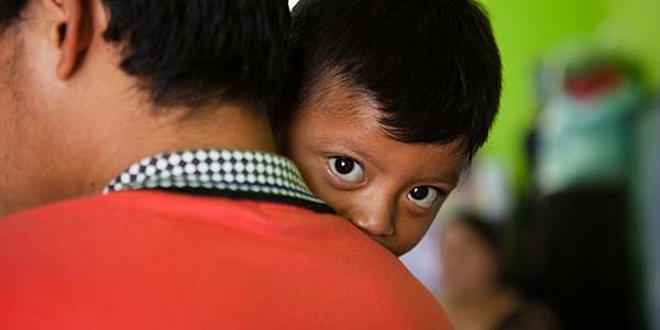 3-year-old Esbin peeks at us over his father’s shoulder in an emergency shelter.