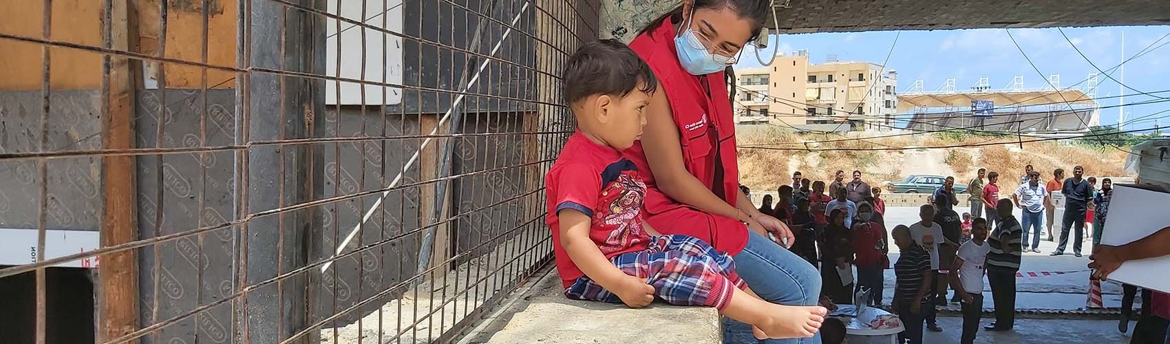 In Lebanon, a health worker wears a face mask while sitting besides a young boy on a ledge overlooking the town.