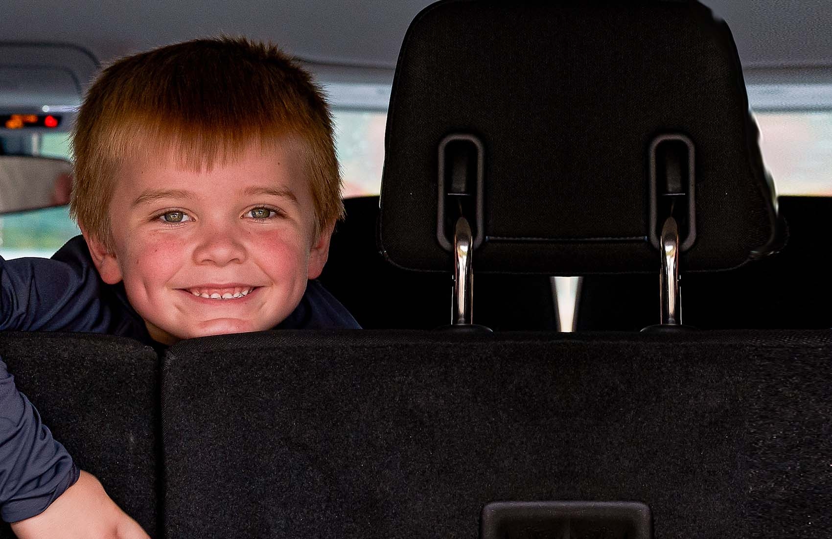 A boy smiles while looking out the back of a car while receiving food during COVID-19.