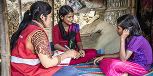 A Save the Children staff member sits with two adolescent girls.