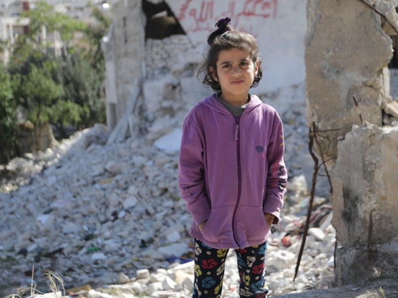 A young girl stands amid the rubble in Syria