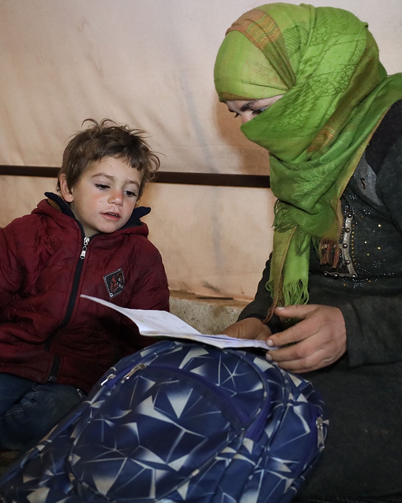 A young boy in Syria sits with his mother looking at schoolwork