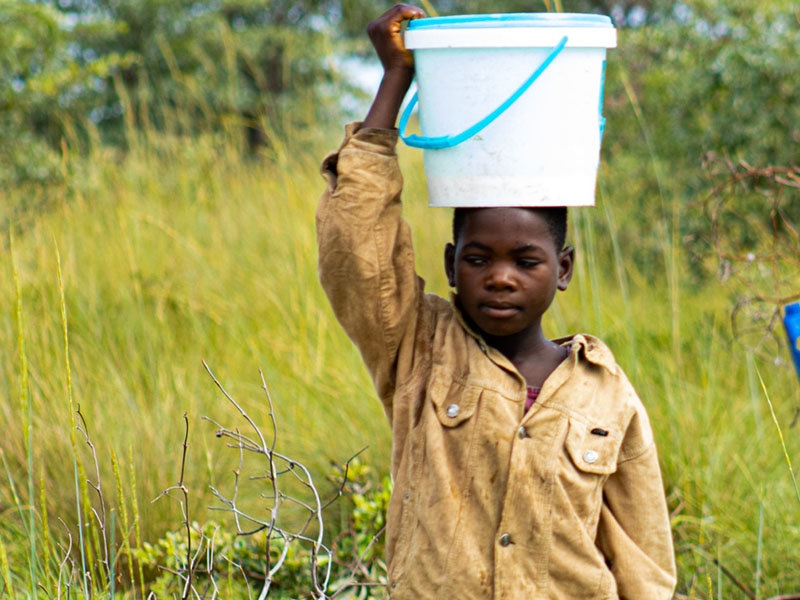 In Zambia, a girl carries water in a bucket back to her home