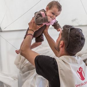 A worker holds a child in a Save the Children tent