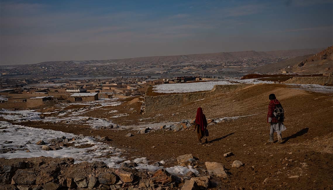 Two children walk outside in a vast area of Afghanistan.