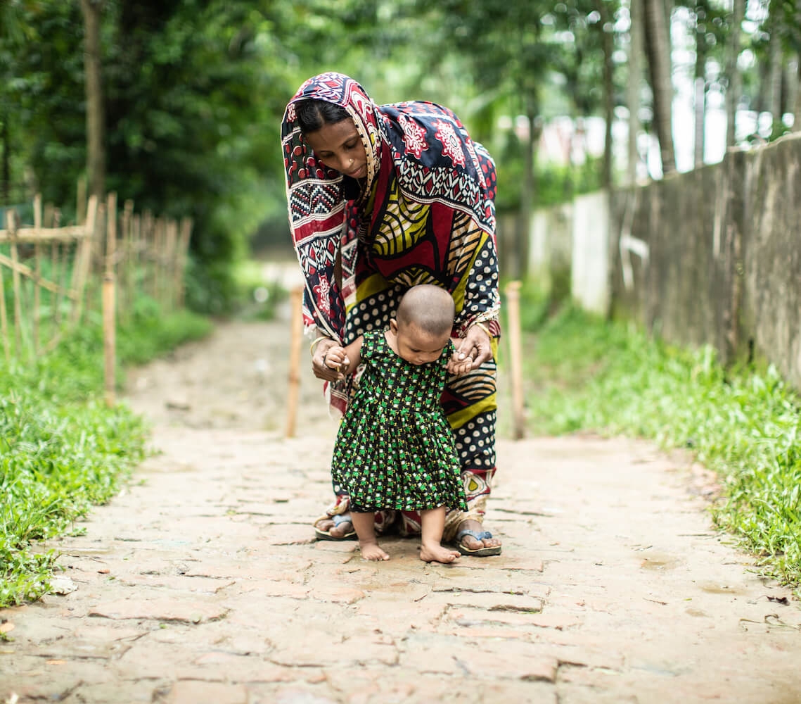 Bangladesh, a mother helps her toddler walk down a path