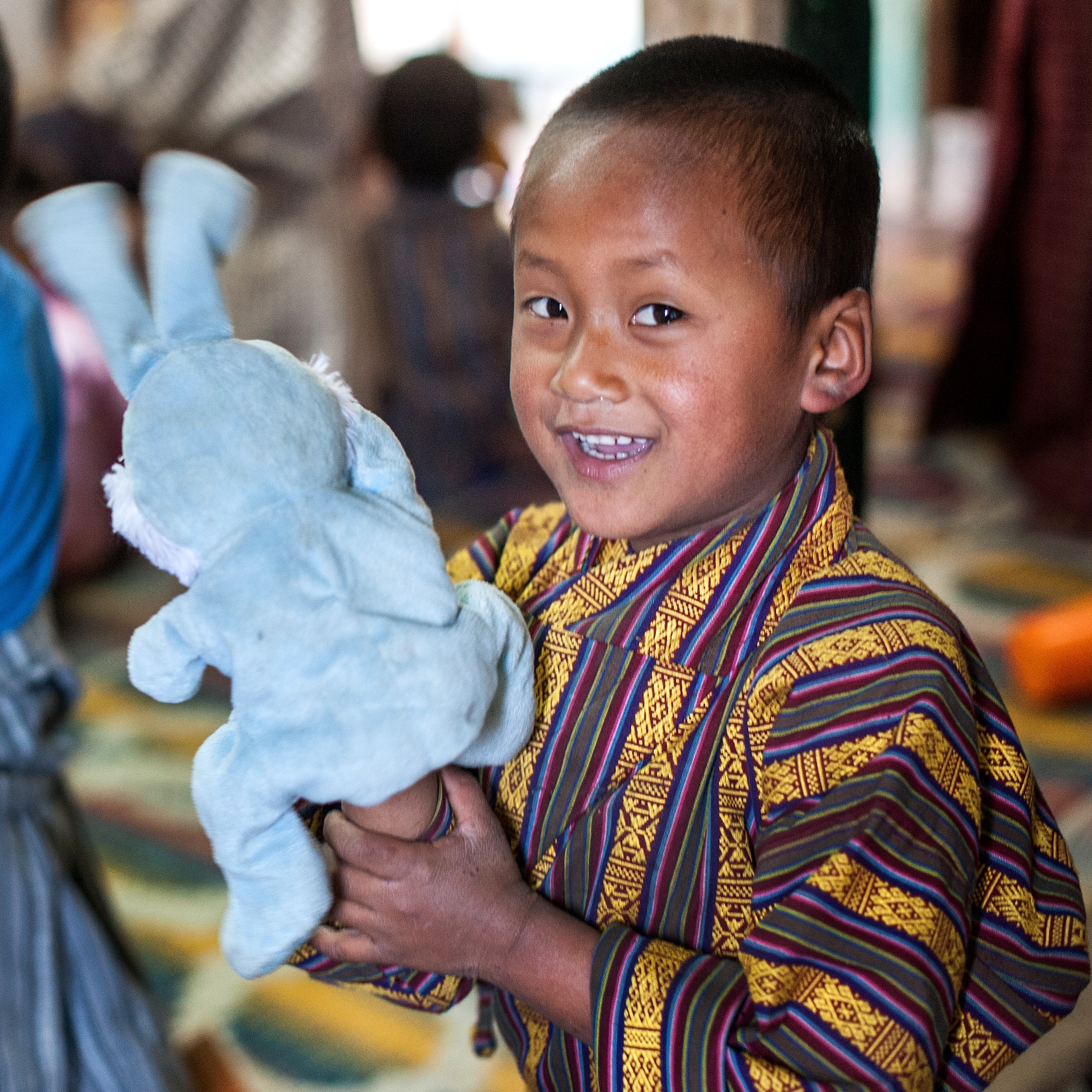 Pema smiles for the camera and holds up a rabbit stuffed animal. He and his friend Chimi are using their imaginations in a learning corner, set up at a preschool in Bhutan. The Red Nose Day Fund helped Save the Children improve the quality of education in more than 200 preschools in Bhutan, training teachers to incorporate play-based math and reading activities that help increase school readiness. Photo credit: Susan Warner/Save the Children, March 2016. 