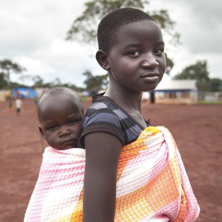 A young girl in Burundi carries a small child on her back using a cloth sling. 