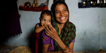 At a home in India, a mother rests her hand on her daughter while laughing and smiling.