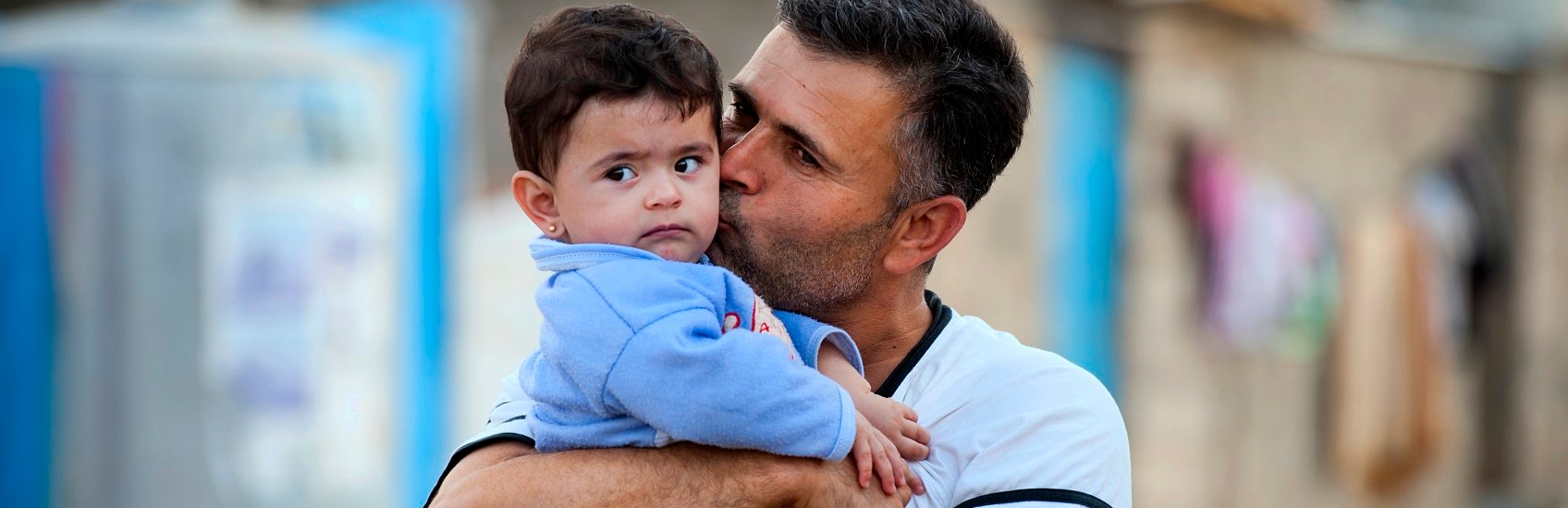 A fourteen month-old boy get a kiss from his father at a refugee camp. Hundreds of thousands of refugees and internally displaced families have fled the violence across Iraq and Syria. Children in Iraq have often witnessed or experienced violence, and left their homes in terrifying circumstances. Many now face hot summers and freezing winters living in tents, half built apartment blocks and public buildings. Save the Children is providing essential goods to families, such as water and hygiene kits, as well as building sanitation facilities and running child friendly spaces and education classes. Photo credit: Sebastian Rich/Save the Children, October 2014.