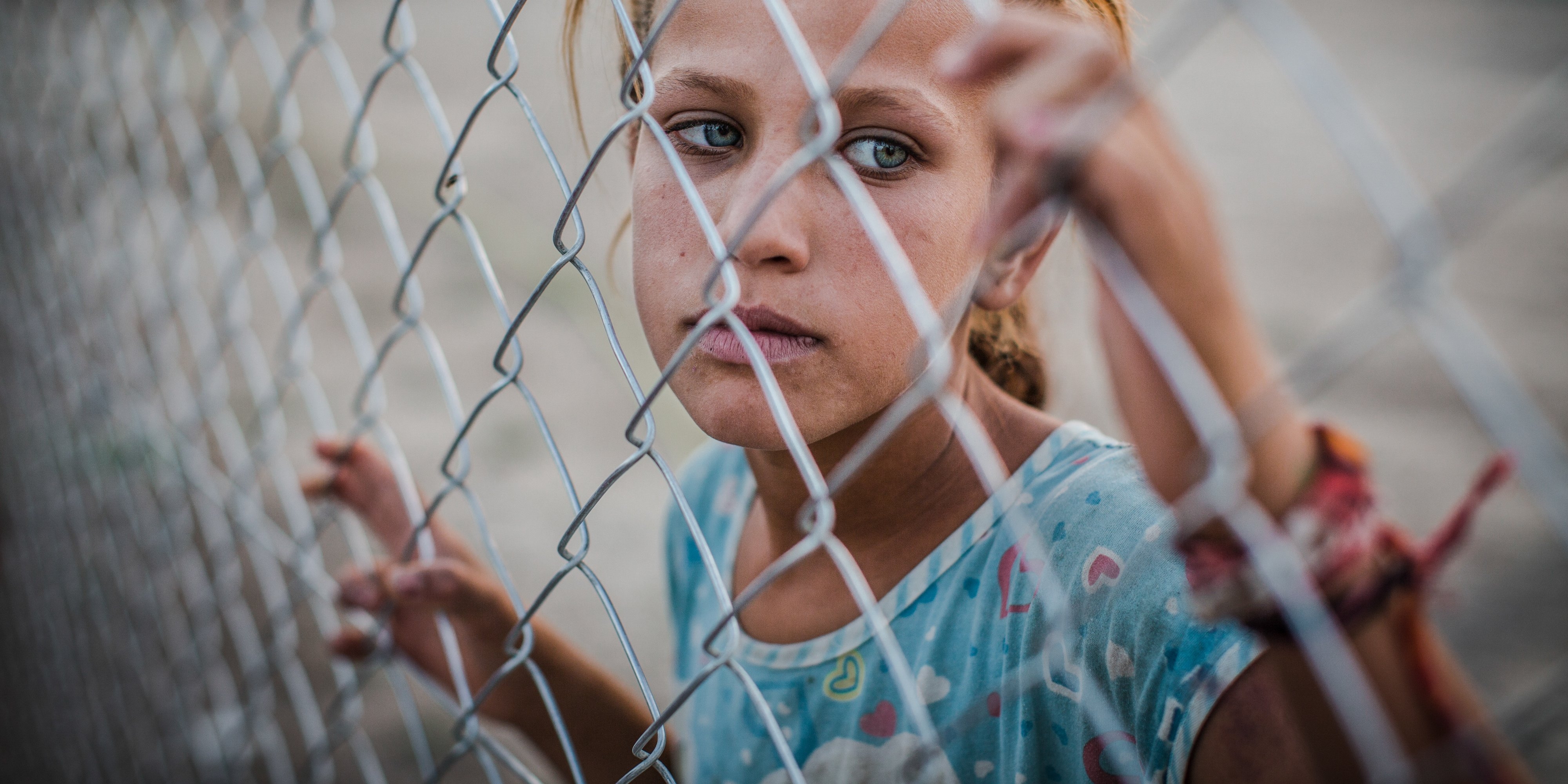 A young girl stands behind a fence at a refugee camp. She and her family are among the 3.1 displaced people in Iraq. Due to armed conflict the family of eight, were forced to leave their home and flee. Photo Credit: CJ Clarke/Save the Children 2015.