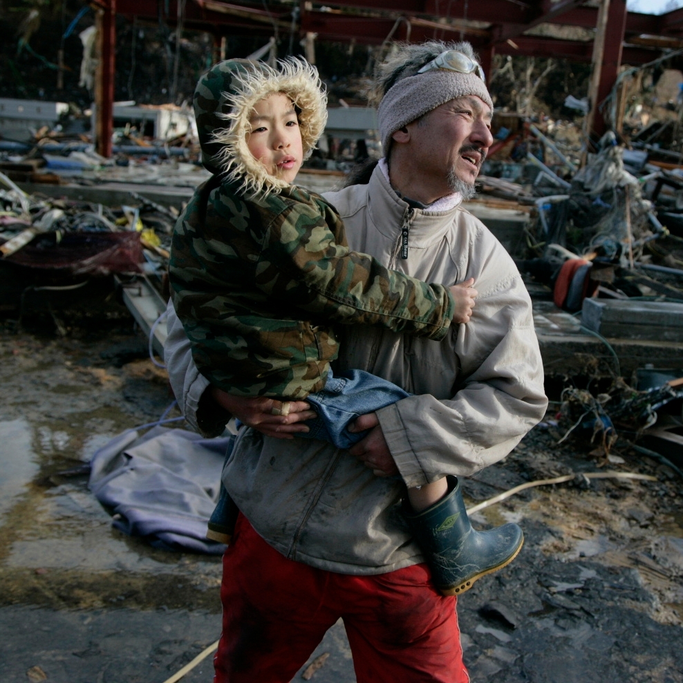 Hirohiko Oka and his son Suzunosuke, age 6, walk through the rubble of Onigawa, Japan on March 16th to see the remains of their home after two tsunami waves devastated their town. Photo Credit: Jensen Walker/Getty Images for Save the Children 2011.