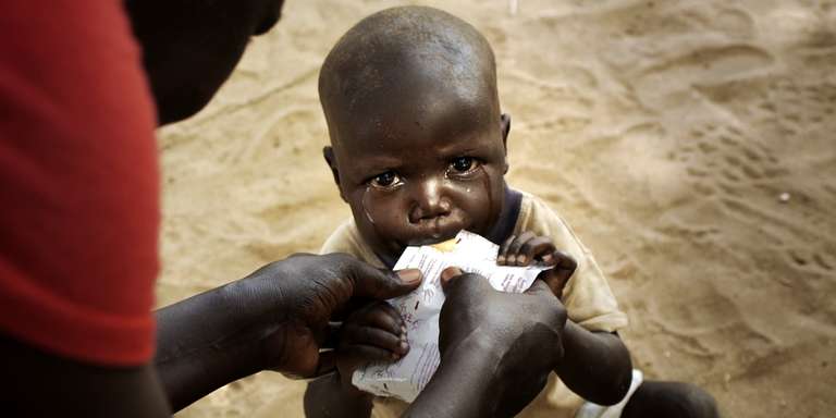 An 18 month-old child hungrily eats therapeutic food from a pouch as tears stream down his face. This young child is being treated for malnutrition in his village in Turkana County Kenya. Community health worker Cecilia Akai gives him a MUAC test and ready to use high-nutrient peanut paste. Save the Children is supporting the Ministry of Health to effectively deliver and manage High Impact Nutrition Interventions (HINI) to mothers and children in Turkana County. Photo credit: Allan Gichigi/Save the Children, July 2016.