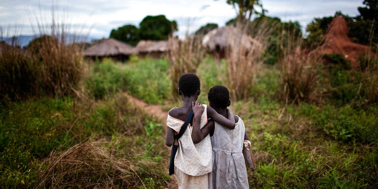 In Mozambique, two young children face away from the camera and look out over a village.