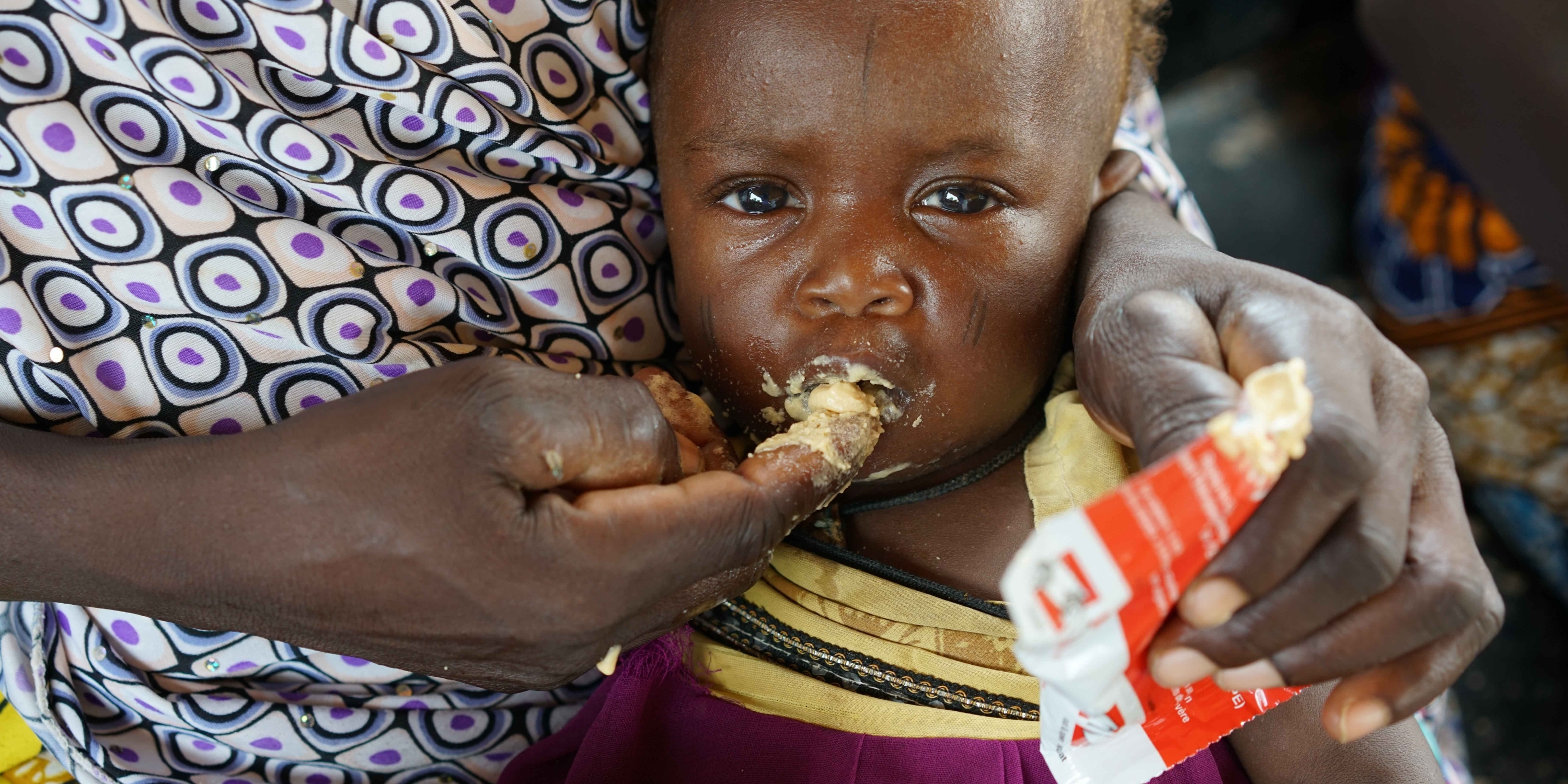 An infant of 9 months, with her mother Alima, eats high nutrient peanut paste as a distribution at the Guidanaoutchi Clinic, Niger. Photo Credit Save the Children 2016.