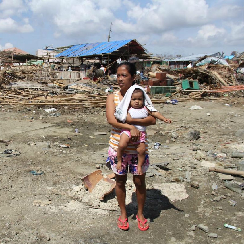 Philippines, a mother holds a baby in front of rubble caused by a natura disaster