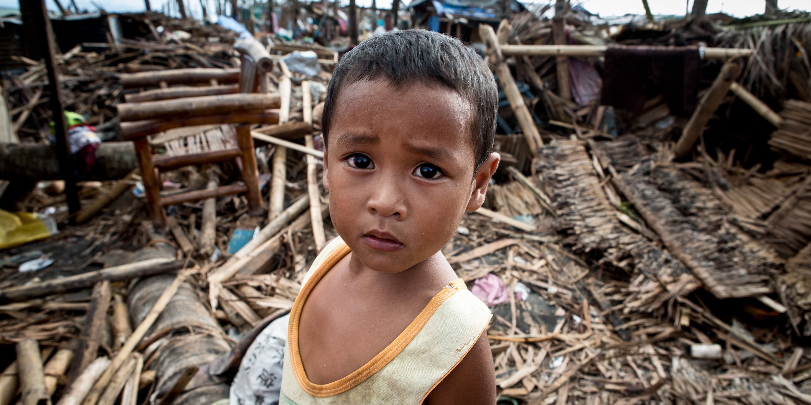 Kirby, four, stands amongst the debris where his house once stood before it was destroyed by typhoon Haiyan, Philippines. Photo Credit: Jonathan Hyams/Save the Children 2013
