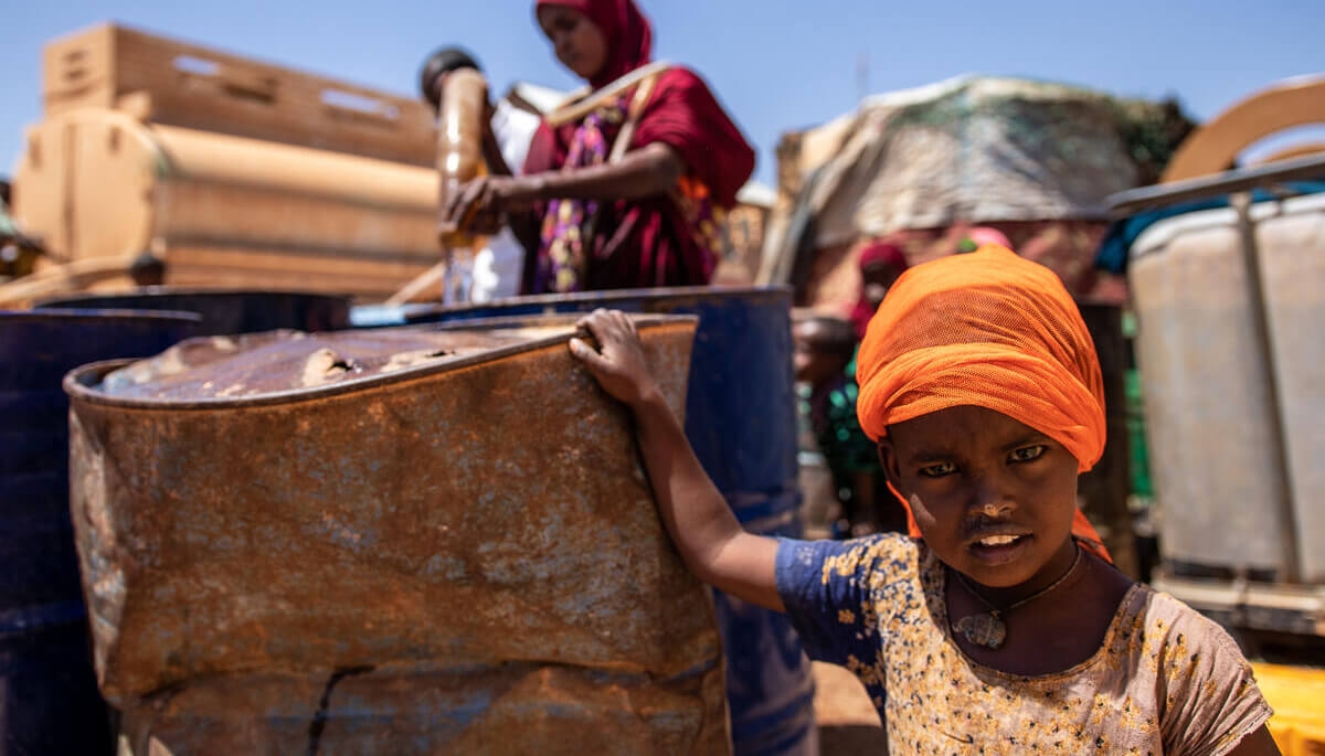 In drought-ravaged Somalia, a girl stands near a water bucket.