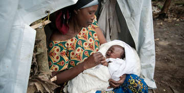 A foster mother, Theresa, cradles a newborn in a refugee settlement of Rwamwanja, Uganda. Theresa has 3 children of her own, but is helping care for the baby and her 5 siblings after the mother died from childbirth complications. The children’s father – a solider – was in a military hospital after being shot in the leg amid violence in the Democratic Republic of the Congo. Photo credit: Rebecca Vassie/Save the Children, March 2014. 