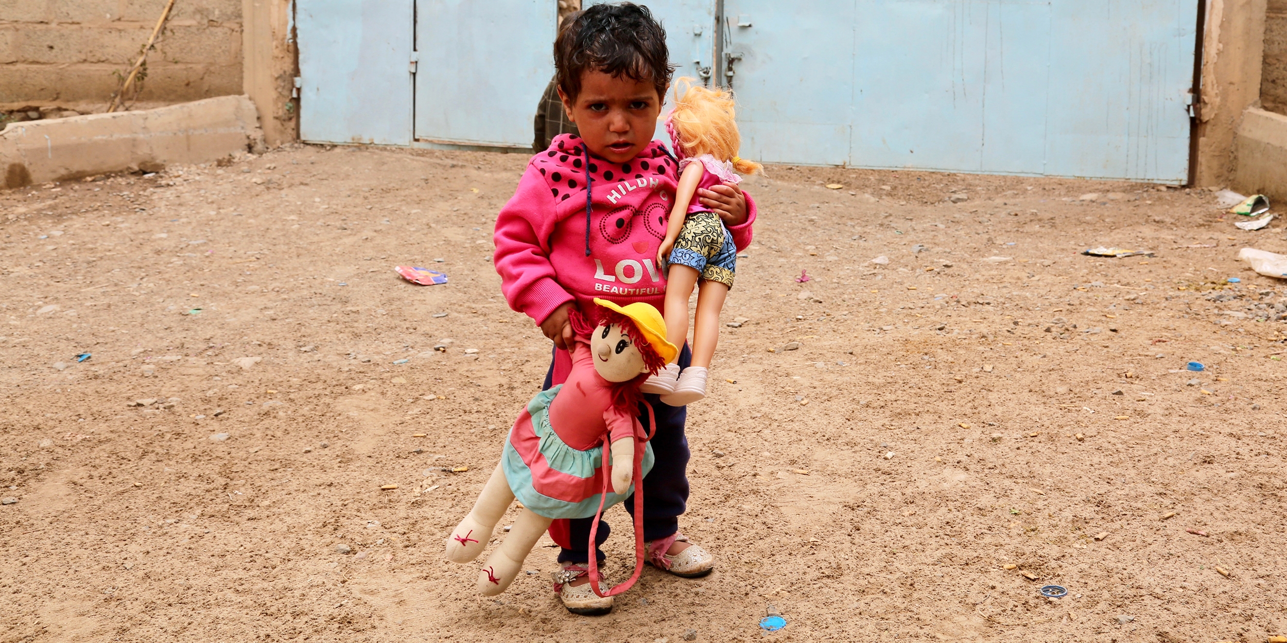 A Yemeni child holds their dolls outside