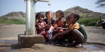 A group of children gather around a water spigot