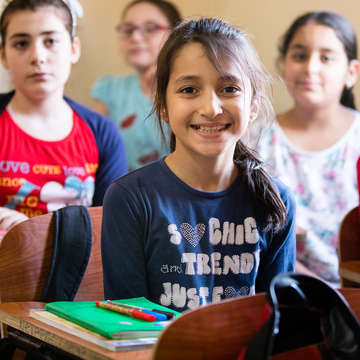 A 10-year old sponsored girl smiles from her desk in a classroom. She is part of Save the Children's refugee sponsorship program in Egypt and is one of four child ambassadors within the program. She and her family are Syrian refugees who fled their country in 2012 in hopes of a better life. Thanks to Save the Children's refugee sponsorship program, both short-term and longer-term needs of vulnerable refugee children and their families are addressed, including protection, education, health and livelihoods support, counseling and psychological support. Photo credit: Victoria Zegler / Save the Children, October 2017. 