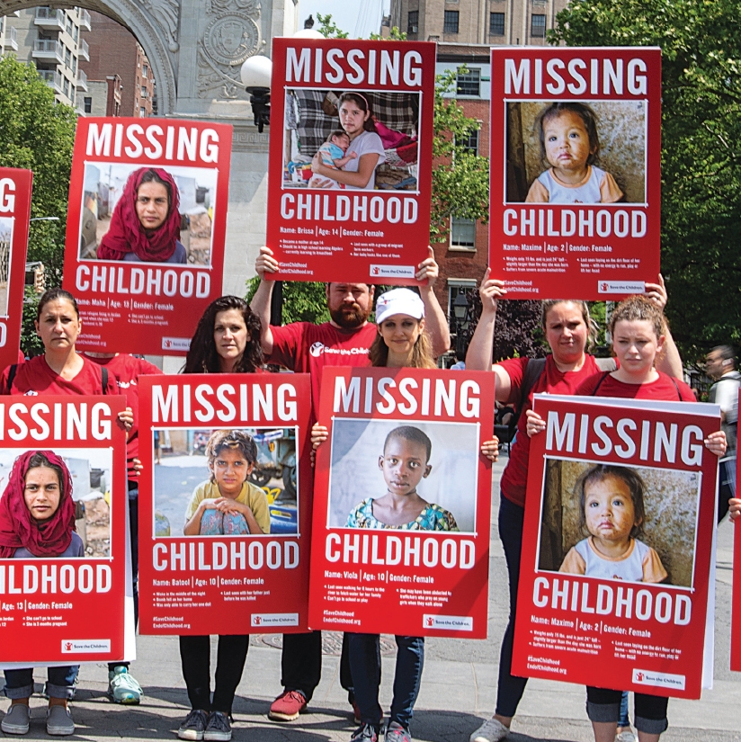 A group of Save the Children voluneers holding up signs that bring attention to children who miss out on childhood. 