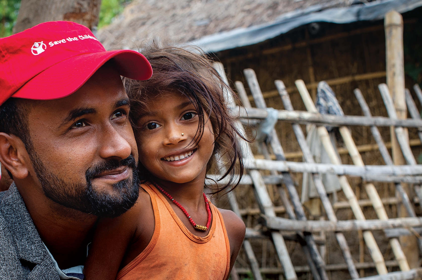 Nepal, a Save the Children worker smiles with a cute little girl in an orange shirt