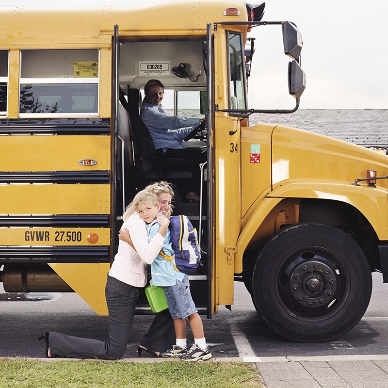 Parent and child hug in front of a yellow school bus