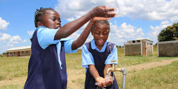 Hannah enjoys clean water with her friend. Photo credit: Save the Children 2020.