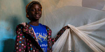 Gniré poses for a photograph with a mosquito net. Photo credit: Save the Children 2018.