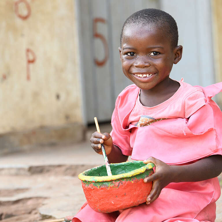 A young girl holding a bowl and smiling at the camera. 