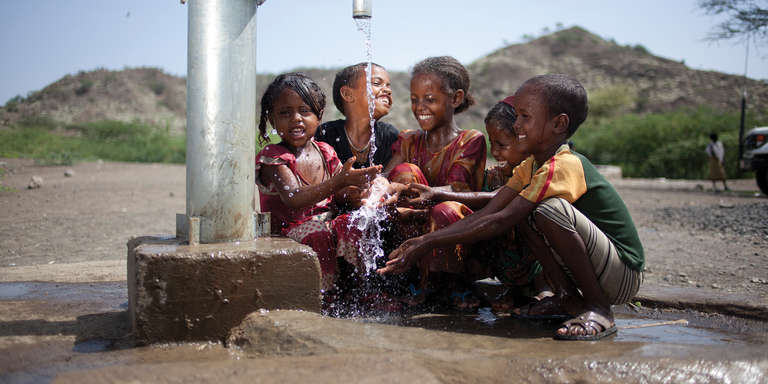 A group of children play in a water spigot