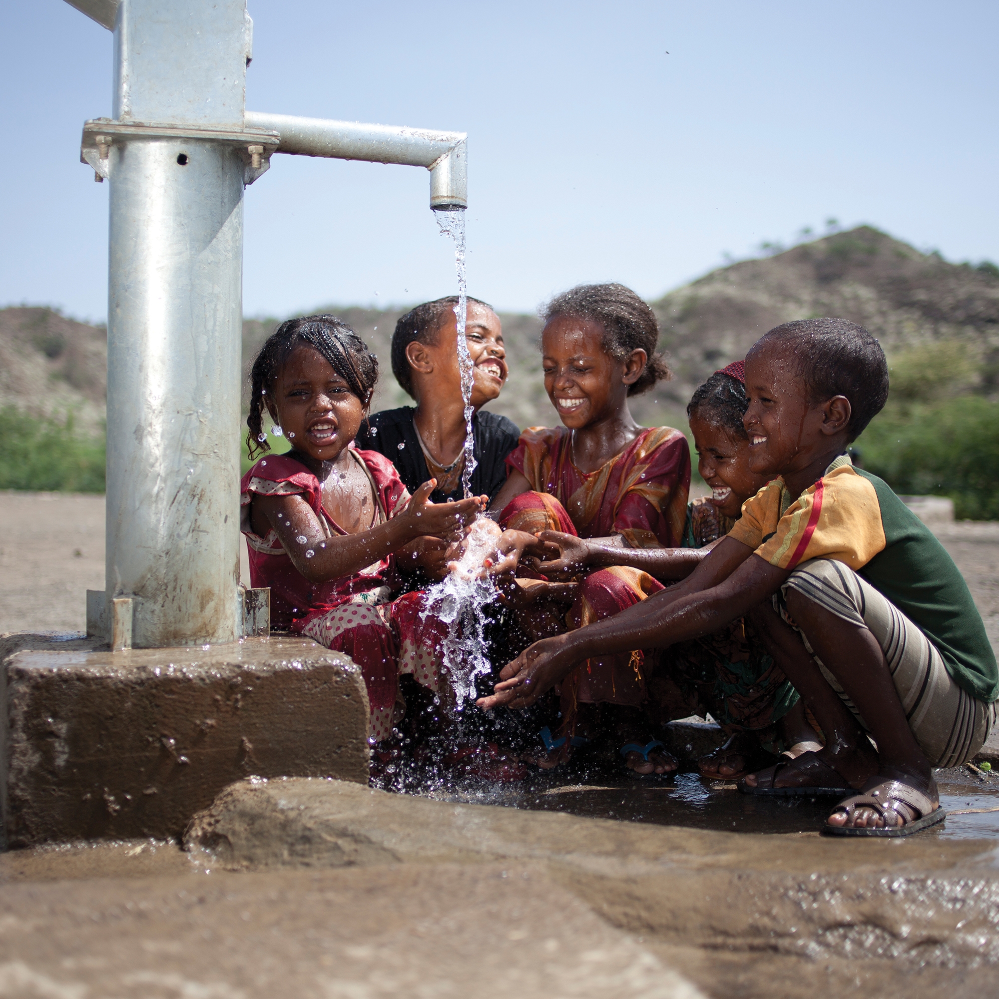 Children gather around a water pump. 