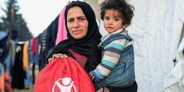 A mother stands with her child holding a refugee family comfort kit. 
