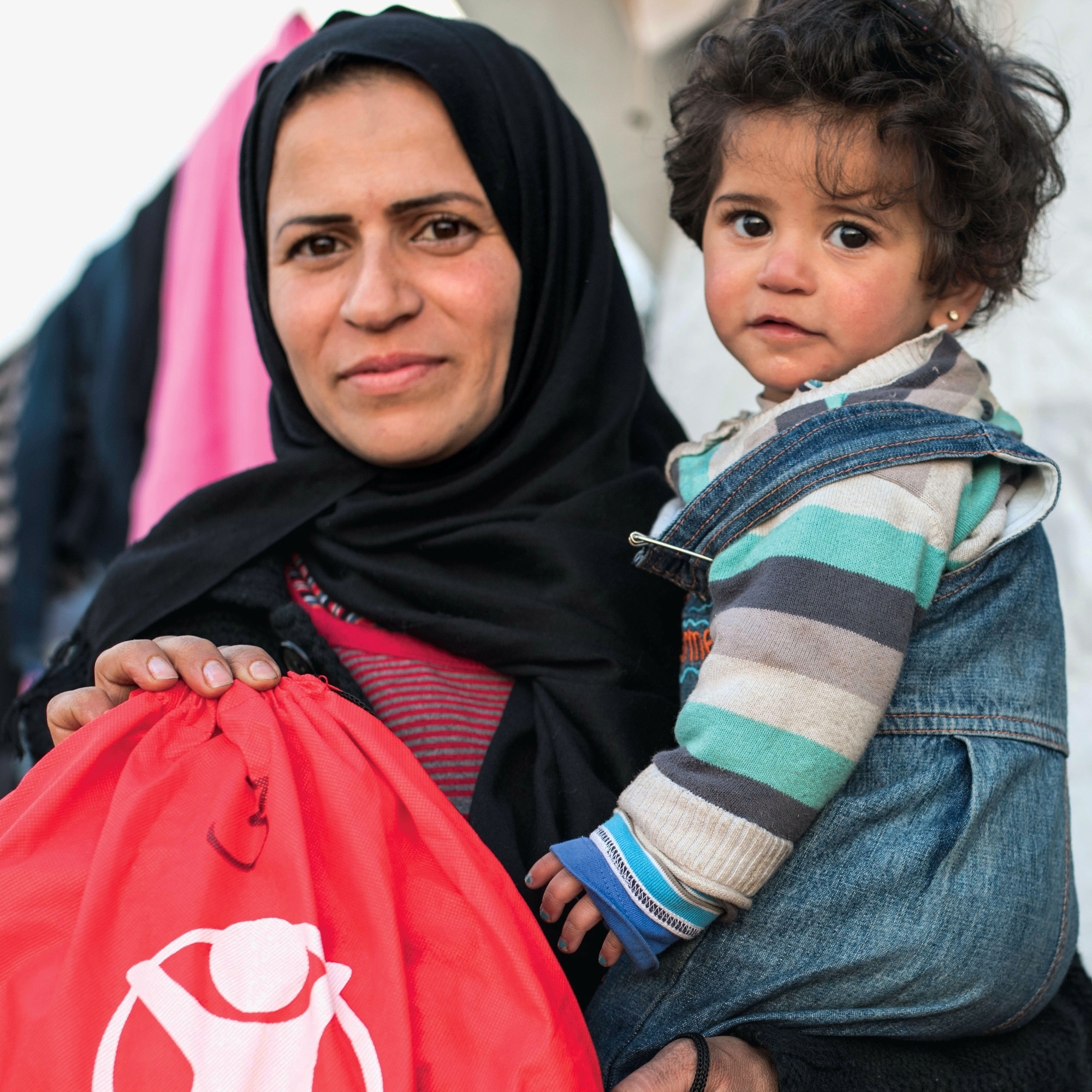 A caregiver holds a baby and a Save the Children backpack.