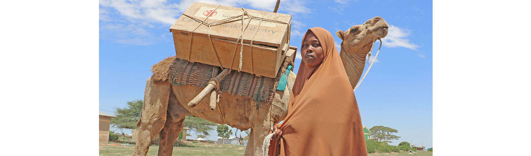Maha, 13, is holding the lead to a camel, which carries a portable library on its back.
