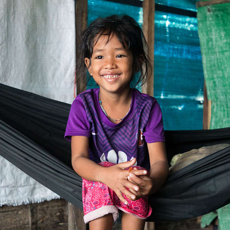 Five-year-old Seima sits on a hammock inside her floating home on the Tonle Sap Lake in Cambodia. Behind her, the walls are merely tarps. Her floating village has a floating pre-school, which she loves. She travels to the school by boat, and there she learns to read, sing and count. Save the Children trains teachers, provides teaching materials and pays to help rebuild the school, which is needed every year due to the water. Photo credit: Hanna Adcock / Save the Children, October 2018. 