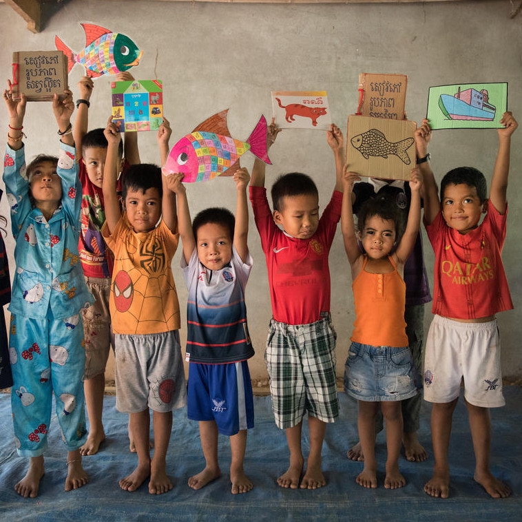 Children stand with their hands above their heads, happily holding favorite books and drawings.