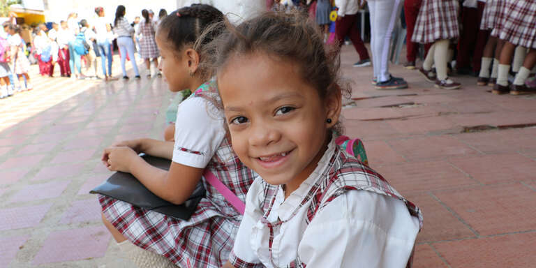 A girl smiles while sitting next to a friend in Colombia. 